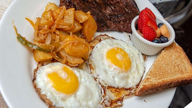 Fried eggs with homefries, steak, fresh fruit and toast