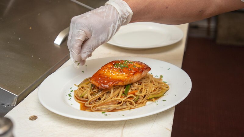 Chef sprinkling herbs on salmon with pasta entree